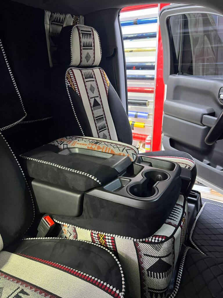 A car interior featuring premium upholstery with a seat cover adorned in intricate tribal designs.