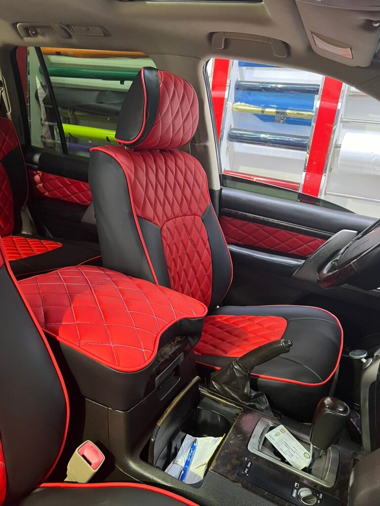 A car interior with luxurious red and black leather seats, showcasing the ongoing work at Al Badiya Car Accessories & Upholstery.