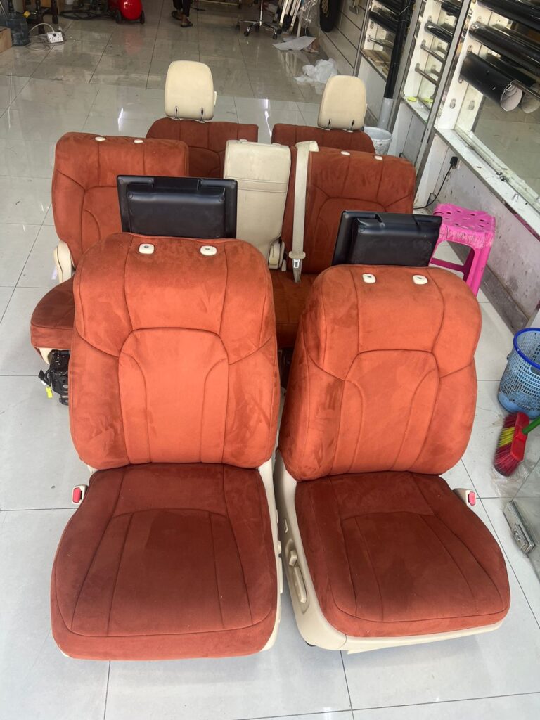 Six orange and tan car seats are displayed at "AlBadiya Car Accessories & Upholstery," showcasing their progress on upholstery work.