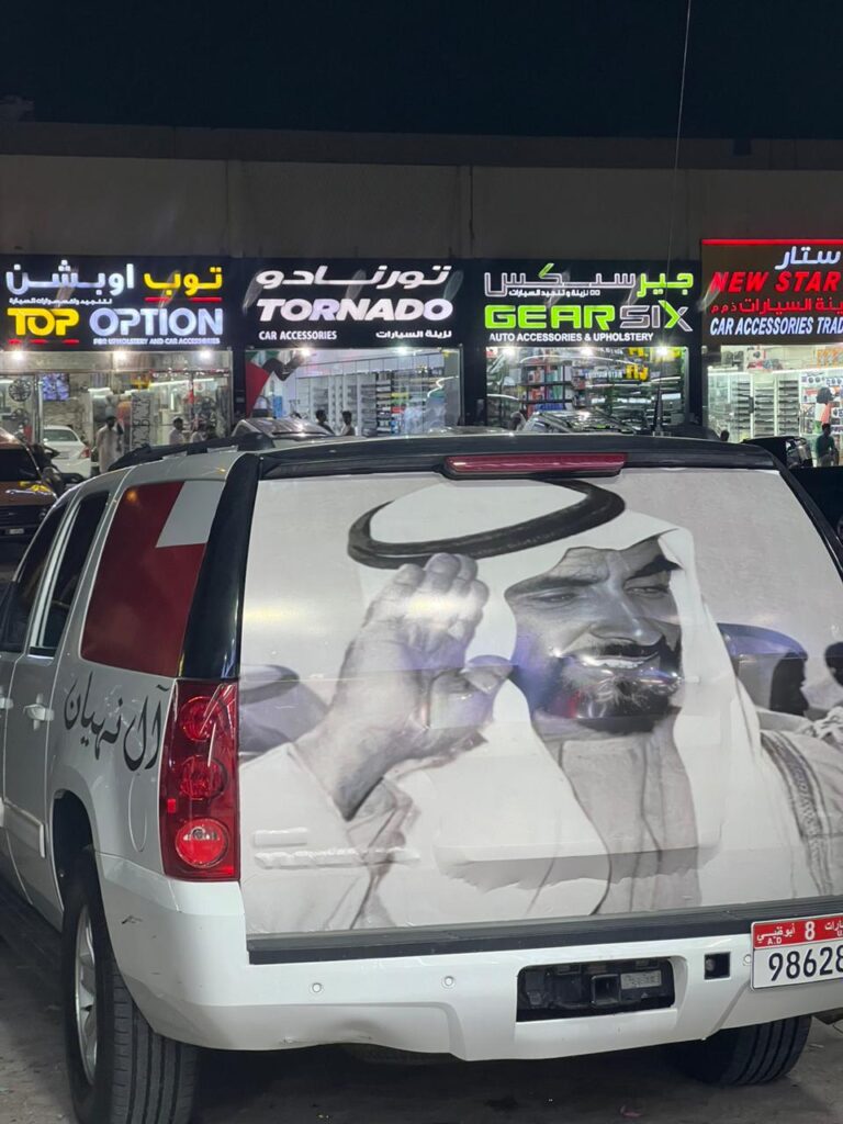 A truck with a vibrant car wrap prominently displays a large image of Zayed bin Sultan Al Nahyan, former president of the UAE.