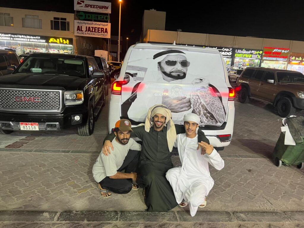 Three men stand in front of a wrapped van, posing for a photo outside AlBadiya shop in Abu Dhabi.