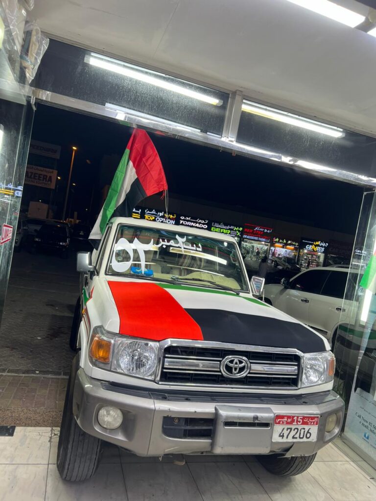 A UAE flag prominently displayed on the roof of a Toyota Land Cruiser symbolizes national pride at AlBadiya shop in Abu Dhabi.