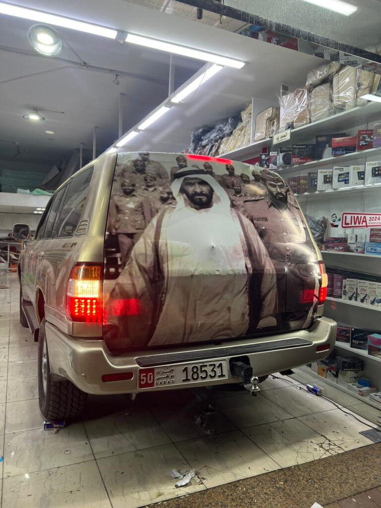 A car with a vibrant wrap features an image of the king of the UAE, demonstrating respect for him.