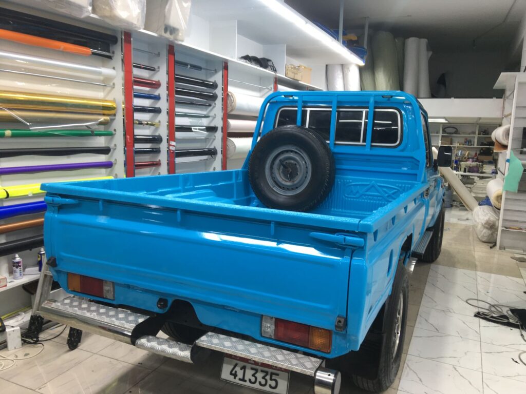 A blue truck featuring a bold car wrap rests in AlBadiya's garage, highlighting its unique style and craftsmanship.