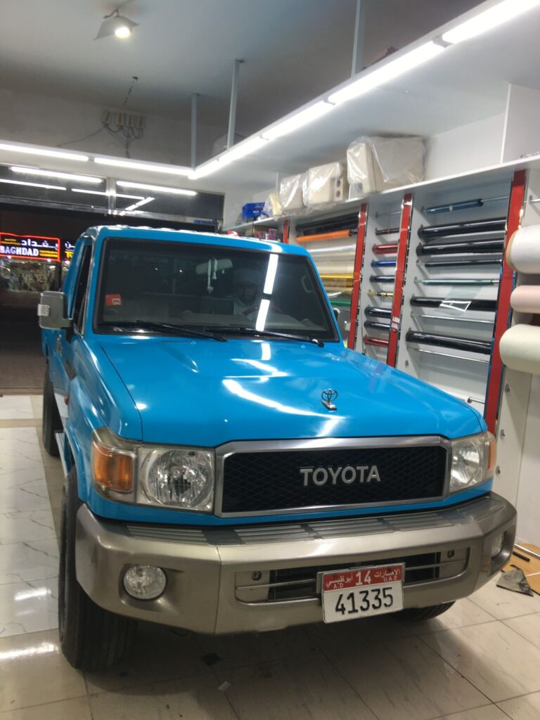 A blue Toyota truck with a car wrap displayed inside the AlBadiya shop, showcasing its vibrant color and design