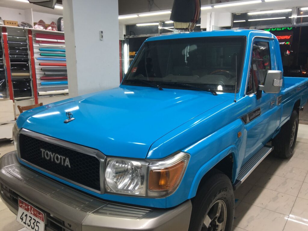 A blue Toyota truck is on display at the AlBadiya showroom, featuring eye-catching car wrapping that enhances its appeal.