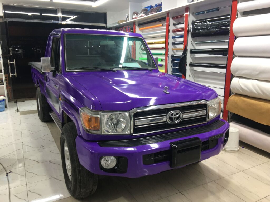 A bold purple Toyota truck adorned with a stylish car wrap, parked in a garage, highlighting its eye-catching design.