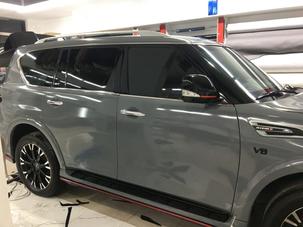 A grey SUV is being expertly wrapped and tinted in a garage, showcasing a transformation in progress.