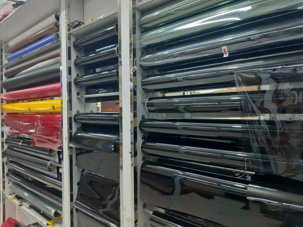 A large rack displaying various colored plastic sheets, including car wrapping and window tinting materials.