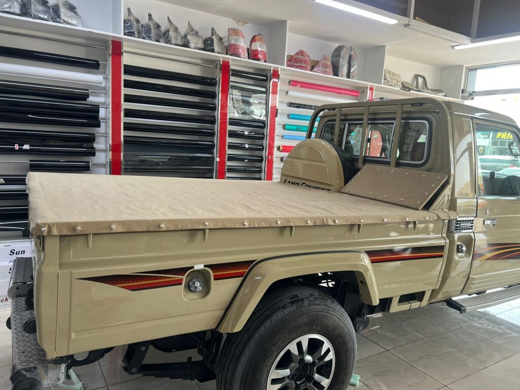 A truck with a bed cover is displayed in the AlBadiya showroom, showcasing a sleek car wrap design that enhances its appearance.