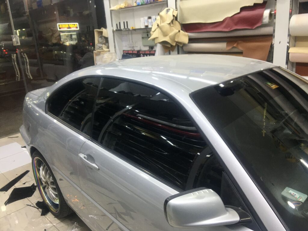 A car is being painted in AlBadiya garage, showcasing window tinting and car wrapping services in progress.