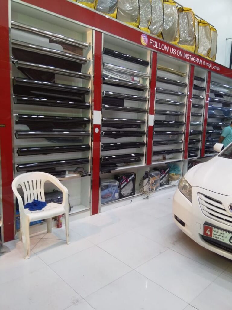 A car work process is taking place in a showroom, surrounded by shelves displaying various car tinting films and accessories.