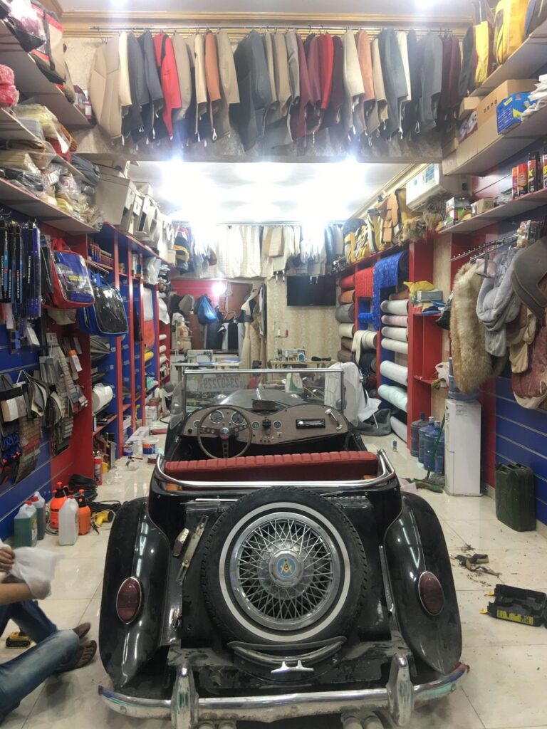 A man diligently repairs a car in a well-organized garage, surrounded by tools and automotive equipment.